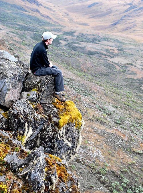 Solo traveler sitting on a rock overlooking the vast plains of Uganda, embracing adventure and nature
