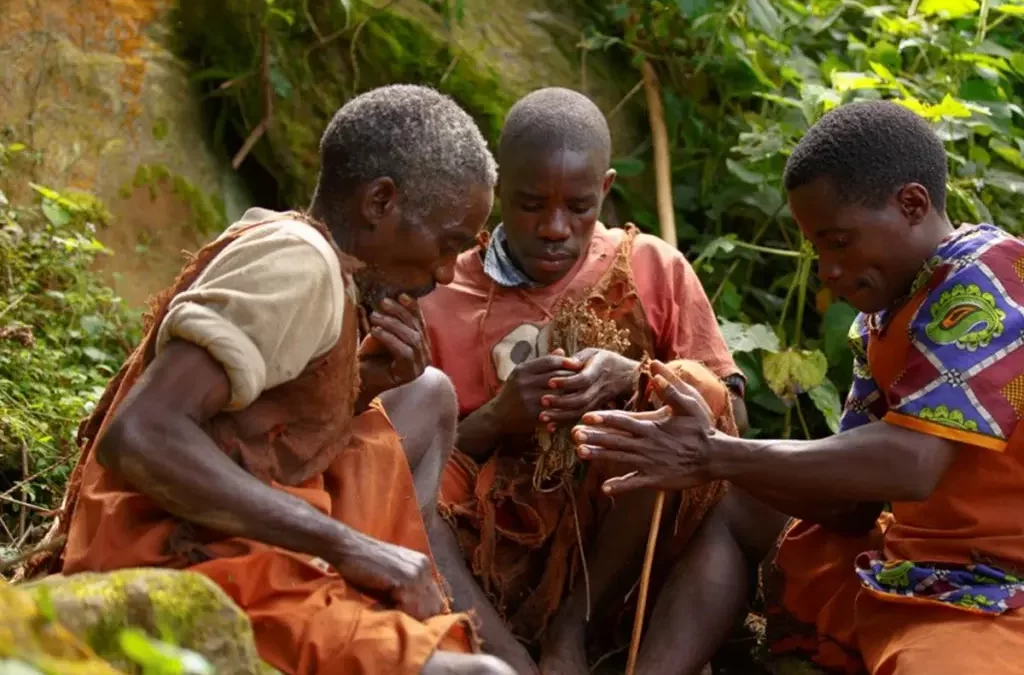 Three Batwa individuals demonstrating traditional fire-lighting techniques during a Batwa cultural experience in Bwindi Impenetrable Forest, Uganda.